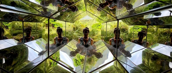 Eine Frau steht am Ende eines Spiegel-Hexagons und blickt hindurch.