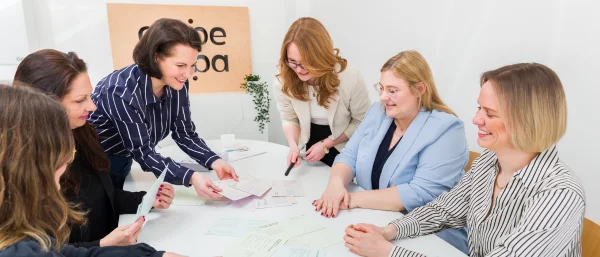 Das Team von Carpe Verba arbeitet gemeinsam an einem Tisch mit verschiedenen Arbeitsmaterialien. Das Bild steht symbolisch für Entscheidungsfindung im Team.
