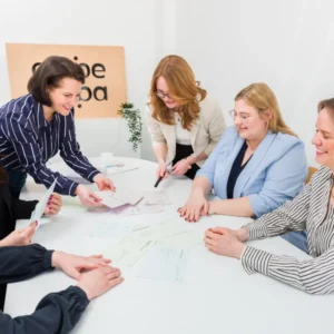 Das Team von Carpe Verba arbeitet gemeinsam an einem Tisch mit verschiedenen Arbeitsmaterialien. Das Bild steht symbolisch für Entscheidungsfindung im Team.