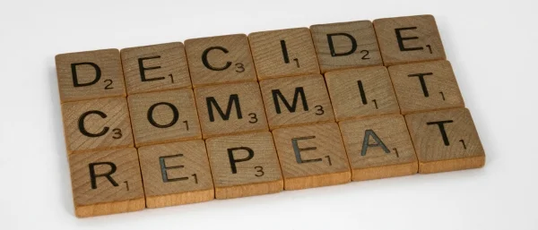 Holblöcke mit Buchstaben bilden die Worte Decide, Comit, Repeat, die als Schritte zur Entscheidungsfindung und Umsetzung von Entscheidungen genutzt werden sollten