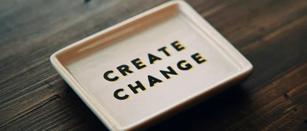 Ein Teller mit der Aufschrift "Create Change" steht auf einem dunklen Holztisch. Das Bild steht symbolisch für das Training "Führen in Change und Transformation".