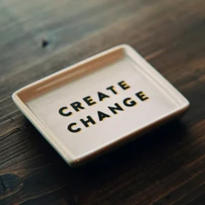 Ein Teller mit der Aufschrift "Create Change" steht auf einem dunklen Holztisch. Das Bild steht symbolisch für das Training "Führen in Change und Transformation".
