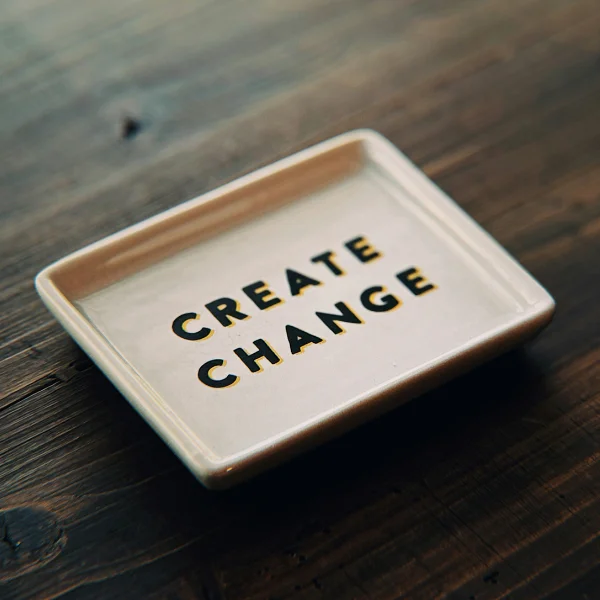 Ein Teller mit der Aufschrift "Create Change" steht auf einem dunklen Holztisch. Das Bild steht symbolisch für das Training "Führen in Change und Transformation".