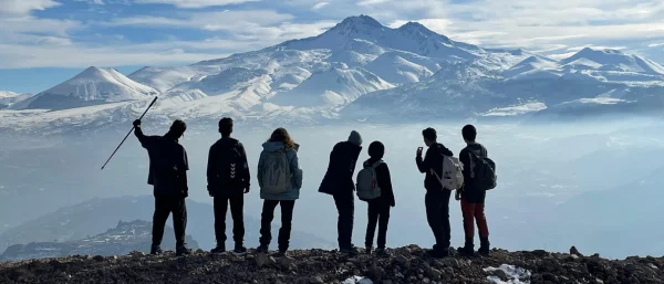 7 Wanderer stehen oben am Gipfel eines Berges und sehen in die Ferne, einer hat den Arm zum Jubel erhoben, steht für die erfolgreiche gemeinsame Entwicklung eines Führungsleitbildes