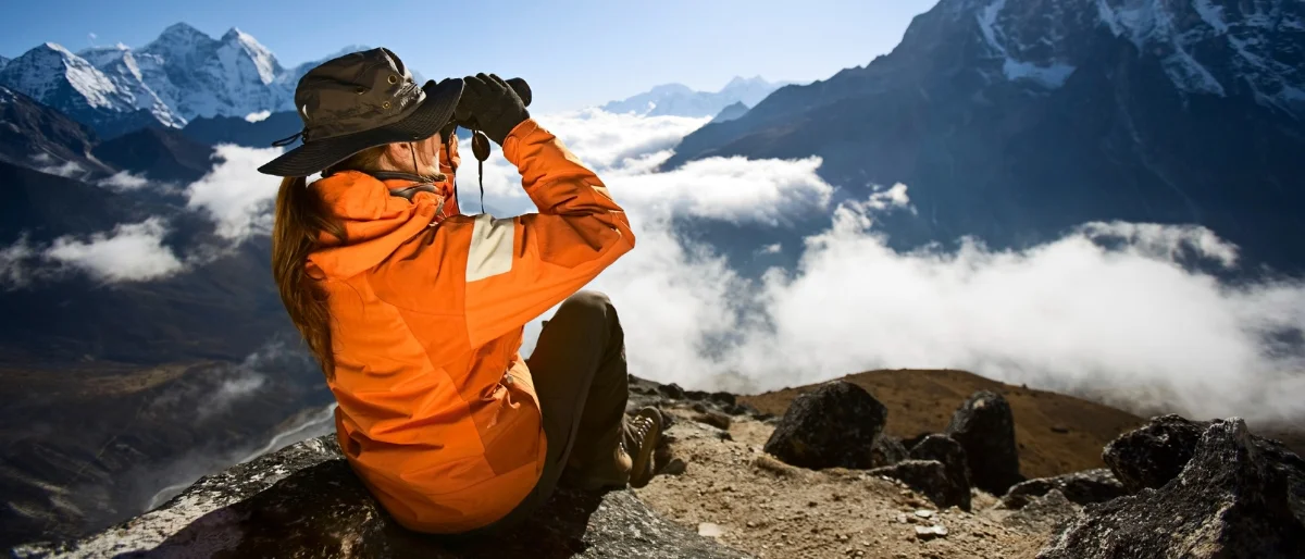 Frau blickt mit Fernglas auf Bergpanorama als Symbol für zukunftsorientierte Prozessbegleitung