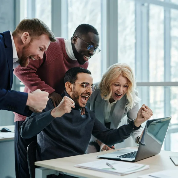 Ein Team sitzt vor einem Laptop und jubelt aufgrund eines Erfolgs.