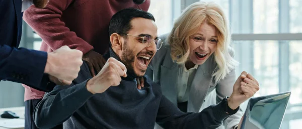 Ein Team sitzt vor einem Laptop und jubelt aufgrund eines Erfolgs.