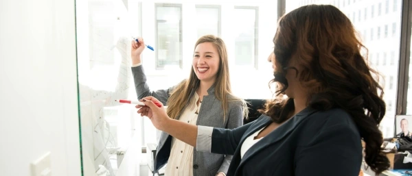 2 Frauen arbeiten an Whiteboard als Symbol für Karriere Coaching