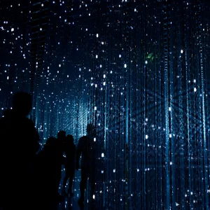 Schatten von mehreren Personen vor einem blau-schwarz leuchtenden Hintergrund, der an zukunftsartige, digitales Leuchten, z.B. von ki / ai erinnert