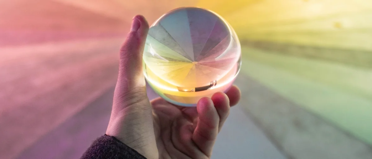 Eine Hand hält eine gläserne Kugel, durch die sich das Licht in einem Spektrum leuchtender Farben bricht. Die Kugel reflektiert und verzerrt die Umgebung auf faszinierende Weise. Das Bild symbolisiert neue Perspektiven, visionäres Denken und den Mut, die Welt anders zu sehen. Es lädt dazu ein, Gewohntes zu hinterfragen und Innovation als kraftvolle Lichtquelle für Veränderung zu begreifen.