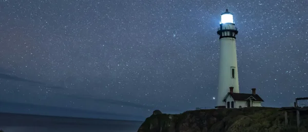 Ein Leuchtturm leuchtet im dunklen. Im Hintergrund sieht man das Meer und einen Sternenhimmel. Das Bild steht symbolisch für die Leitbildentwicklung bei Carpe Verba.