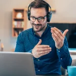 Ein Mann der mit beiden Händen gestikuliert, einen motivierten Gesichtsausdruck hat und vor einem Laptop sitzt. Scheinbar ist es ein erfolgreicher Live-Online-Termin