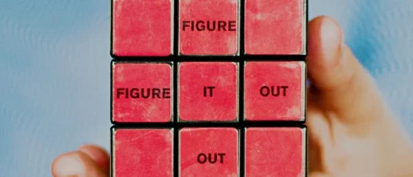 Die rote Seite eines gelösten Rubik's Cube wird von einer Hand vor hellblauem Hintergrund gehalten. Auf dem Würfel steht "Figure it out".