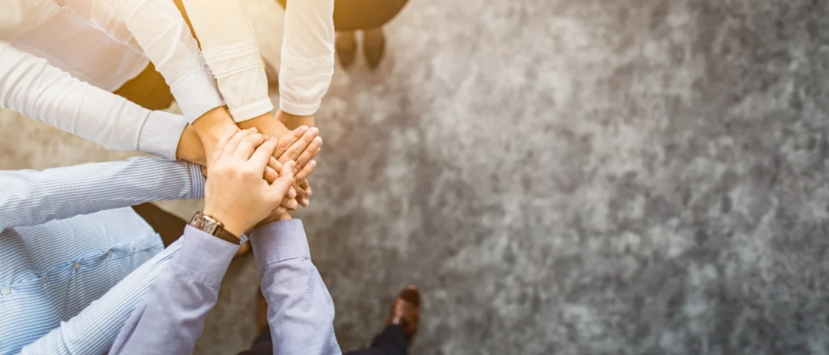 Psychologische Sicherheit im Team wird dargestellt durch übereinander gelegte Hände von mehreren Mitarbeitenden.