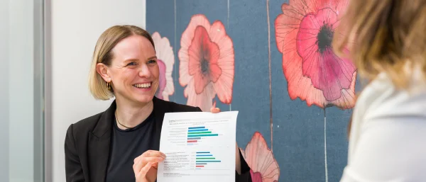 Jana Schmid - Trainerin bei Carpe Verba - ist im Austausch mit einer ihr gegenübersitzenden Person und hält ein Blatt in der Hand, das sie der Person zeigt.