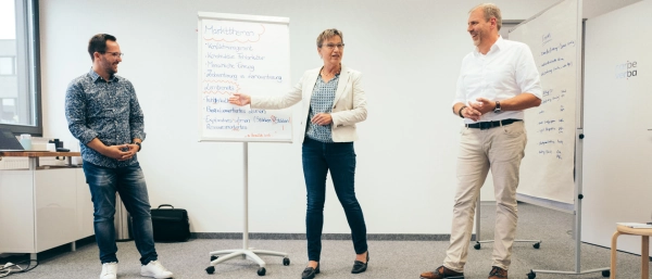 Zwei Trainer und eine Trainerin von Carpe verba! stehen im Seminarraum in Regensburg und diskutieren aktuelle Themen der Organisationsentwicklung und Personalentwicklung.