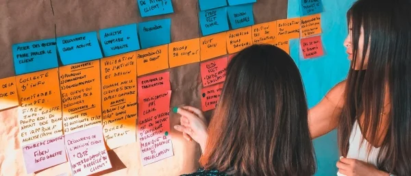 Zwei Personen stehen vor einer Pinnwand mit Post-its, um Aufgaben verantwortungsvoll nach Rollen zu teilen