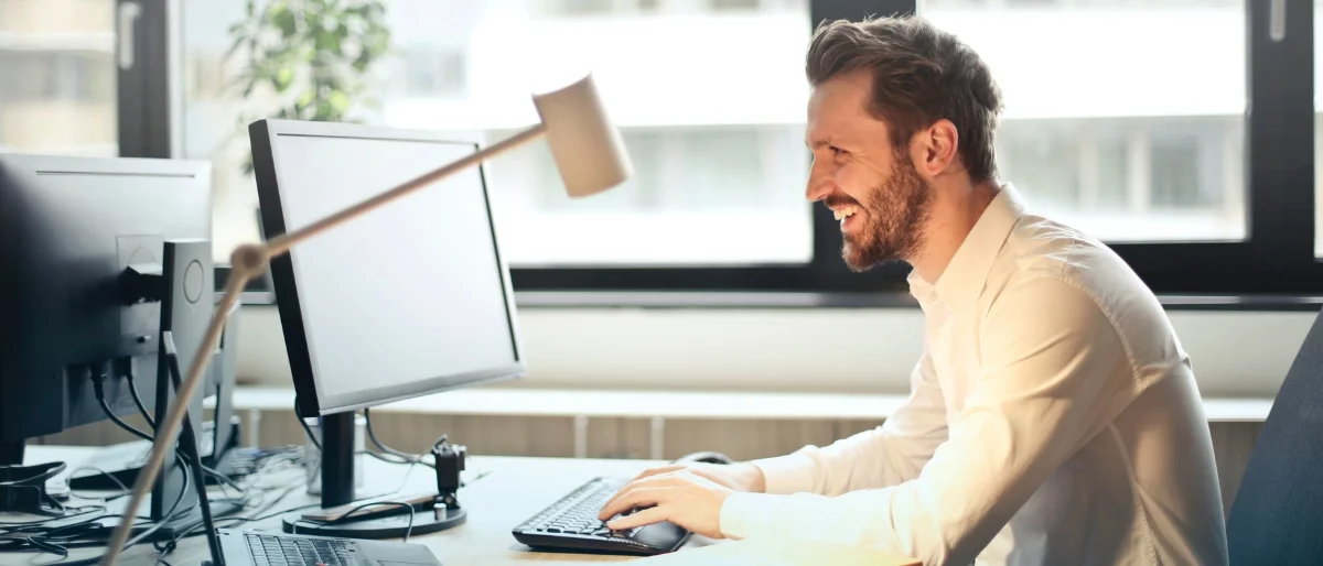 Motiviert wirkender Mann vor einem Bildschirm und einer Schreibtischlampe, der voller Elan an einem Online-Meeting teilnimmt