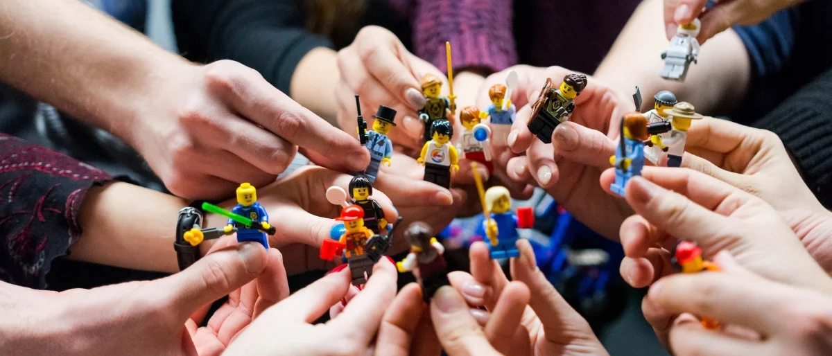 Hände halten verschiedene Lego-Figuren – Symbol für kreatives Storytelling, Teamarbeit und das Entwickeln von Geschichten durch interaktive Methoden.
