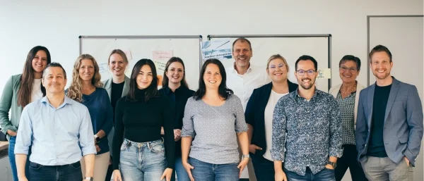 Das Team von Carpe verba! steht als motivierte Gruppe vor einer Pinnwand weil es sich über neue Praktikant*innen im Bereich Training und Coaching in Regensburg freut