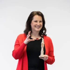 Frau präsentiert mit einem Lächeln eine Figur – Symbol für Storytelling, emotionale Kommunikation und wirkungsvolle Präsentationstechniken.
