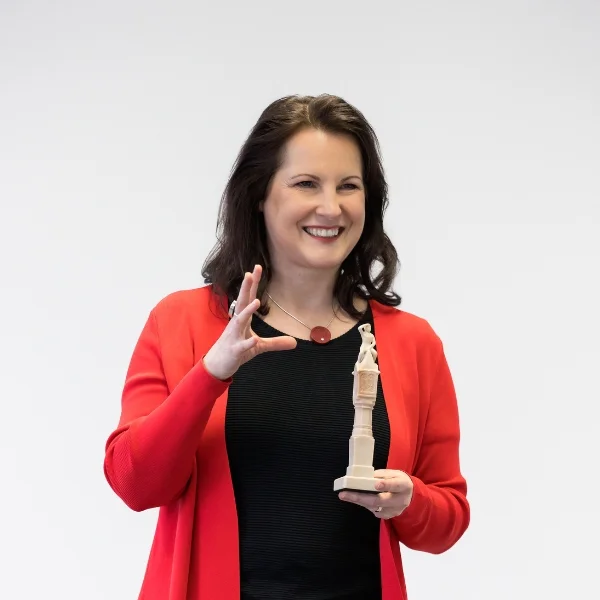 Frau präsentiert mit einem Lächeln eine Figur – Symbol für Storytelling, emotionale Kommunikation und wirkungsvolle Präsentationstechniken.
