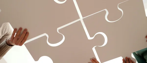 Mehrere Puzzle-Teile werden von Menschen gemeinsam zusammengefügt, steht für ein Weiterbildungsangebot in der systemischen Beratung