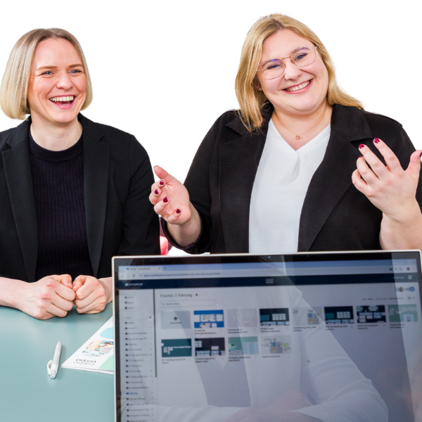 Jana Schmid und Bettina Golba sitzen an einem Tisch und führen ein Gespräch. Im Vordergrund ist ein Laptop mit einer geöffneten Präsentation zu sehen. Das Bild zeigt eine Szene aus der Arbeit von Carpe verba! im Bereich Personalentwicklung und Organisationsentwicklung in Regensburg.