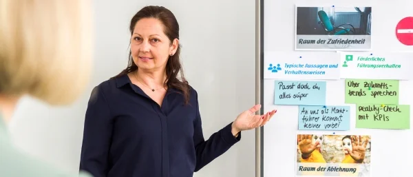Kathrin Schloderer von Carpe verba! Regensburg erläutert in einem Seminar zur Personalentwicklung und Organisationsentwicklung Inhalte an einer Pinnwand mit farbigen Karten und Bildern.