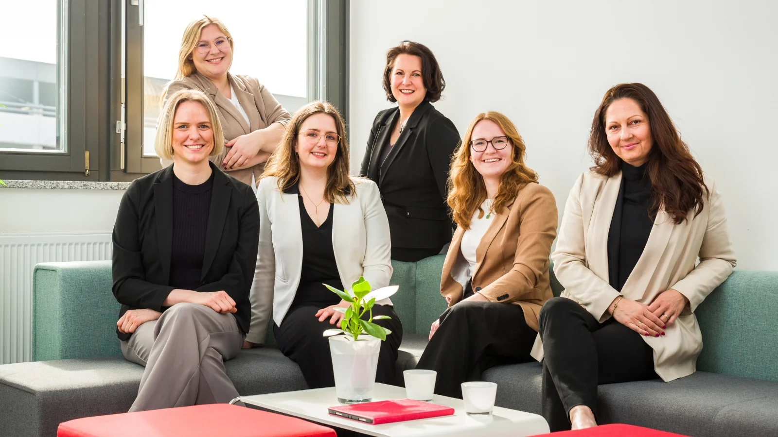 Das Team von Carpe verba! sitzt und steht gemeinsam in einem modernen Besprechungsraum und blickt freundlich in die Kamera. Carpe verba! begleitet in Regensburg Unternehmen in der Personalentwicklung und Organisationsentwicklung.