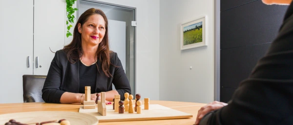Kathrin Schloderer - Trainerin bei Carpe Verba - sitzt vor einem Brett mit Holzfiguren und unterhält sich mit einer ihr gegenübersitzenden Person. Das Bild steht für Coaching bei Carpe Verba.
