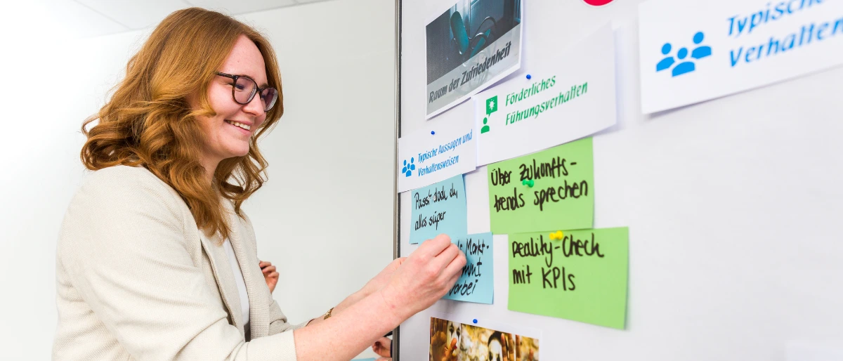 Marlies Voggenreiter - Trainerin bei Carpe Verba - lächelt freundlich und pinnt Moderationskarten an die Pinnwand.