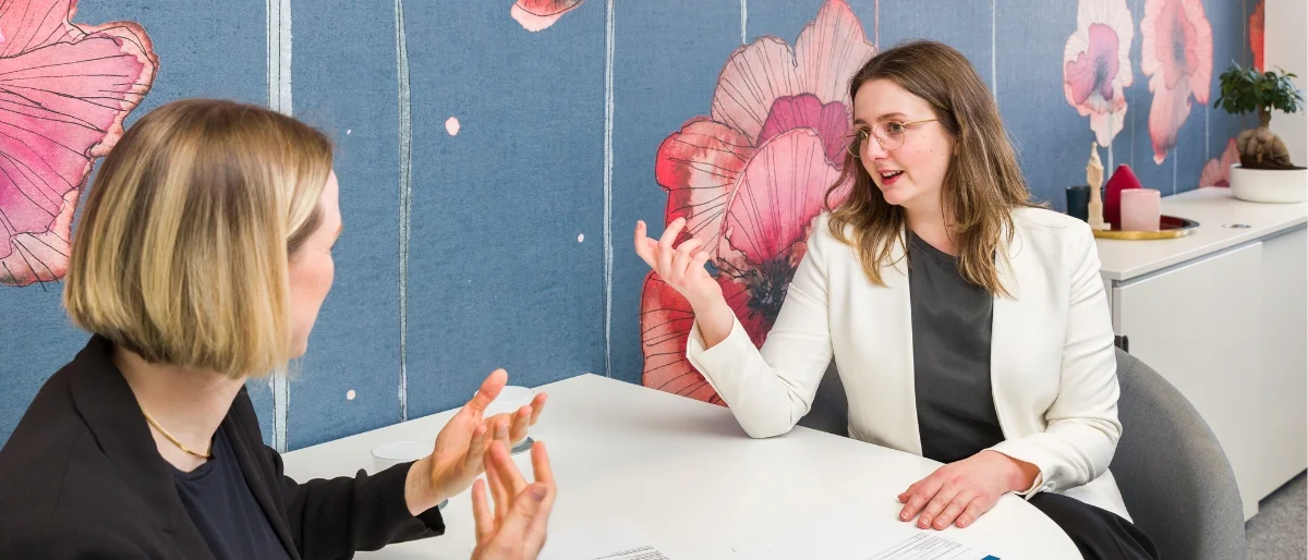 Führungskraft sitzt mit Teammitglied gemeinsam am Tisch, beide haben die Hände erhoben