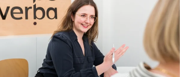 Frische Führungskraft im Gespräch mit Mitarbeitenden am Tisch, die Hand gestikulierend erhoben