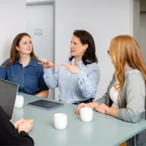 Vier Frauen im Gespräch an einem Besprechungstisch bei Carpe verba, eine erklärt mit lebhafter Geste, die anderen hören aufmerksam zu.